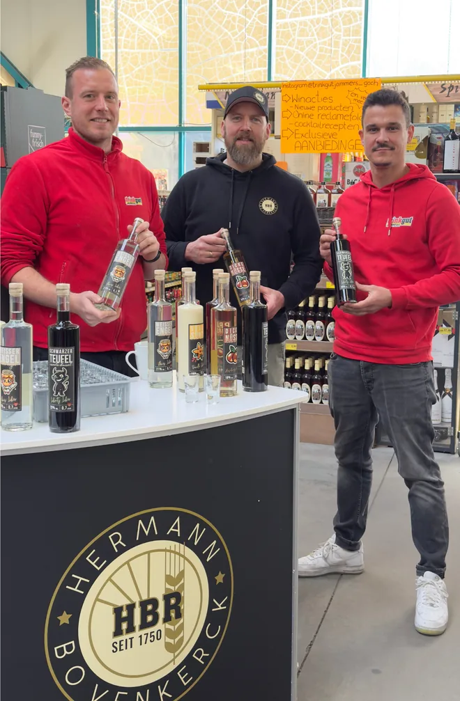 Drie personen met likeurflessen bij een proeftafel in de winkel