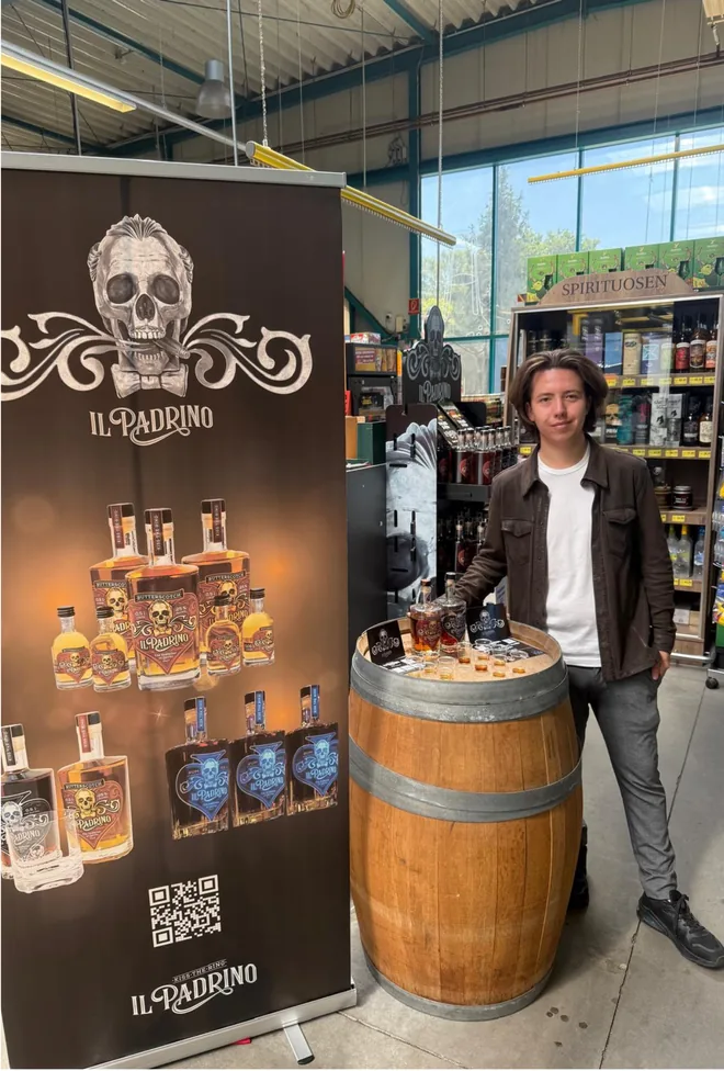 Een persoon bij een houten vat met Il Padrino-flessen en proefglazen in de winkel