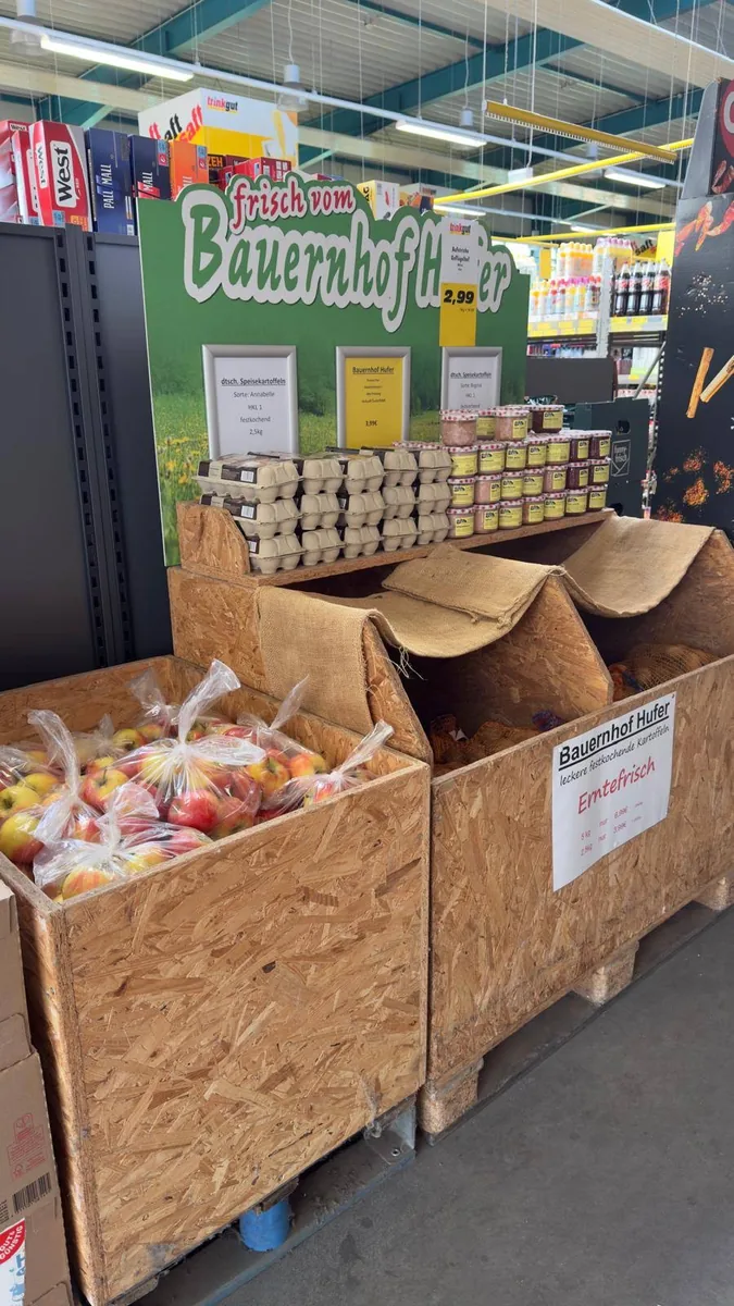 Houten presentatie met appels, eieren en potten onder een groen boerderijbord in de winkel